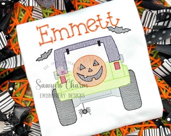 Op de afbeelding: Witte geborduurde T-shirt met de naam "Emmett" en een groene Jeep met een uitgeholde pompoen in de achterbak. De Jeep heeft vleermuizen die erboven vliegen en een spin die aan de achterbumper hangt.