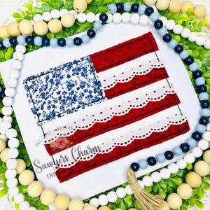 May include: A patriotic square decoration featuring an American flag design. The flag has a blue floral pattern in the corner and red and white striped sections with a scalloped lace trim. The text "Sawyers Charm" is visible.
