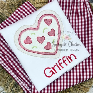 May include: White t-shirt with a red embroidered heart design featuring smaller hearts inside. The text "Griffin" is embroidered in red below the heart.