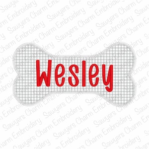 May include: A dog bone-shaped patch with the name "Wesley" embroidered in red. The bone has a gray and white gingham pattern and a white stitched border. The patch is likely for a pet.