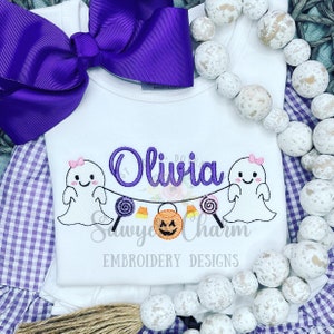May include: White onesie with purple embroidery of two ghosts holding a string of candy, a jack-o-lantern, and the name "Olivia". The text "Sawyer Charm Embroidery Designs" is also embroidered on the onesie.