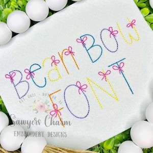 May include: Rainbow font embroidery design with a bow on each letter. The letters spell out "Rainbow Font".