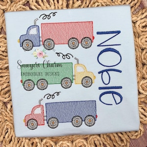 Puede incluir: Una camiseta azul claro con tres camiones de juguete bordados y el nombre "Opie" en letra cursiva azul.