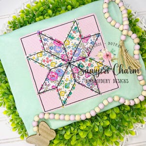 Może przedstawiać: Jasnozielony kwadrat materiału z motywem w kształcie gwiazdy. Gwiazda wykonana jest z kwiatowego materiału i obrysowana czarnymi szwami, umieszczona w różowym kwadracie w kratkę. Widoczny jest tekst "Sawyer's Charm Embroidery Designs".