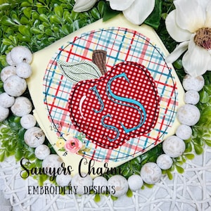 May include: A red apple with a white and blue checkered pattern and a turquoise letter "S" in the center. The apple is surrounded by a yellow, red, blue, and white checkered circle. The text "Sawyers Charm Embroidery Designs" is below the apple.