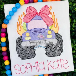May include: White t-shirt featuring a purple monster truck with a pink bow, flames, and large black tires. The text "Sawyers Charm" and "SOPHIA KATE" are also visible. The design is an embroidered graphic.