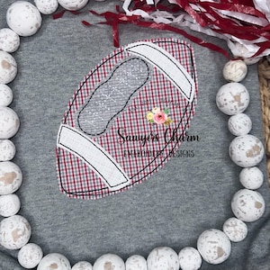 May include: A red and white checkered football with a white outline and a white stitched design. The football is on a gray background with the text "Sawyers Charm Embroidery Designs".
