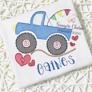 May include: Embroidered design of a blue monster truck with a red heart and the name "Gaines" in blue lettering. The truck has a yellow light and a colorful flag attached to the back. The text "Sawyers Charm Embroidery Designs" is also included.