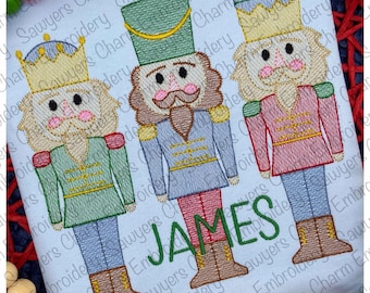 May include: Three embroidered nutcracker figures, one in green, one in blue, and one in red, with the name "JAMES" embroidered below them.