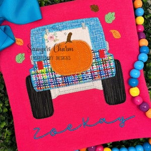 Może przedstawiać: Różowa koszula z haftowanym niebieskim i białym Jeepem, który przewozi dynię. Na koszuli wyszyte są napisy "Sammers Charm Embroidery Designs" i "Zoe Kay".