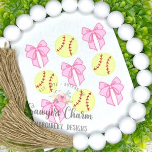 Puede incluir: Un fondo blanco con seis lazos rosas y cinco diseños de softball amarillos. El texto "Sawyer's Charm Embroidery Designs" está en la parte inferior de la imagen.