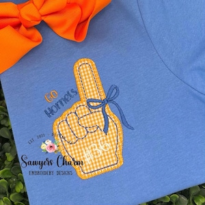 May include: Light blue t-shirt with an embroidered foam finger design. The foam finger is yellow and white gingham with a blue bow. Text includes "Go Hornets" and "#36". An orange bow is in the upper left corner.