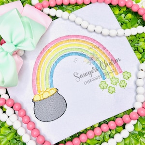 May include: Embroidered rainbow design with a pot of gold and shamrocks. The rainbow features vibrant colors, and the text "Sawyer Charm Embroidery Designs" is visible. A pink and mint green bow is in the upper left corner.