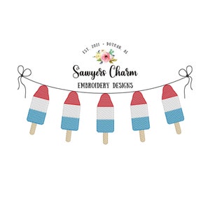 May include: A string of five red, white, and blue popsicle-shaped ornaments hanging from a white string. The ornaments are decorated with a red, white, and blue pattern. The text "Sawyer's Charm Embroidery Designs" is displayed below the ornaments.