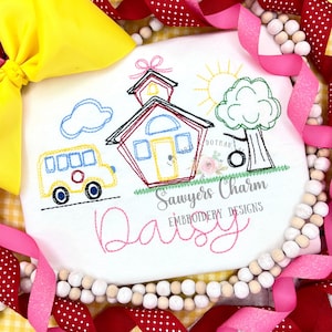 May include: Embroidered design of a schoolhouse, a yellow bus, a tree with a swing, a sun, and a cloud. The text "Sawyers Charm Embroidery Designs" and "Daisy" are also embroidered on the white fabric.