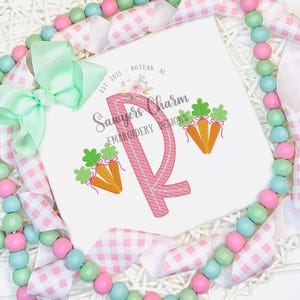 Peut inclure: Lettre "R" brodée en rose avec trois carottes orange et des fanes de carottes vertes. Le texte "Sawyer's Charm Embroidery Designs" est sous la lettre. Le texte "Est 2021 - Dothan, AL" est au-dessus de la lettre.