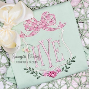 May include: A light green embroidered shirt with a pink bow, a floral design, and the text "EST. 2021 BOTANICAL Sawyers Charm EMBROIDERY DESIGNS" and the letter "IVE" in pink.