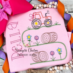 May include: Pink embroidered children's shirt with a tractor, hay bales, and flowers. The text "Little Bit" is embroidered on the shirt. The text "Sawyers Charm Embroidery Designs" is also embroidered on the shirt.