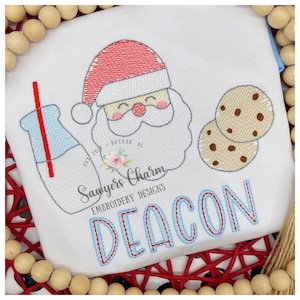 Op de afbeelding: Borduurwerk met de kerstman met een glas melk en een rietje, twee chocoladekoekjes en de naam "DEACON" in blauwe en rode letters. Het ontwerp bevat de tekst "Sawyers Charm Embroidery Designs" en "Est. 2020 - Dothan, AL".