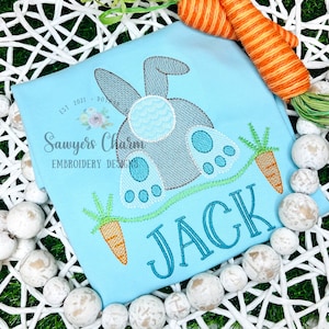 May include: A light blue t-shirt with an embroidered design of a grey bunny rabbit with blue feet and a carrot. The name "JACK" is embroidered in blue below the bunny. The text "Sawyers Charm Embroidery Designs" is embroidered in the top left corner.