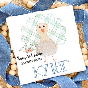 May include: Embroidered design of a turkey with a green and white plaid tail feathers. The design includes the text "Sawyers Charm Embroidery Designs" and the name "Kyler".