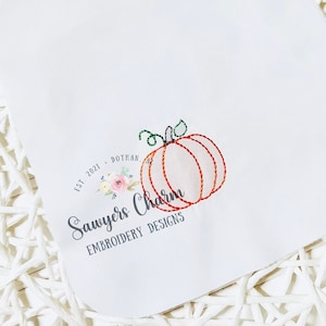 May include: A white background with a logo for "Sawyers Charm Embroidery Designs" featuring a small orange pumpkin with a green stem and leaves. The text "EST. 2021 - DOTHAN, AL" is above the pumpkin.