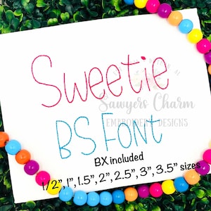 以下が含まれることがあります： ピンクとブルーの刺繍が施された白い布のクローズアップ。"Sweetie BS FONT"と"Sawyers Charm Embroidery Designs"と"BX included 1/2", 1", 1.5", 2", 2.5", 3", 3.5" sizes"というテキストが書かれている。