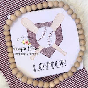 May include: White embroidered baseball themed design with two bats crossed over a maroon home plate and a white baseball. The text "Sawyers Charm Embroidery Designs" and "Leyton" are also embroidered on the design.