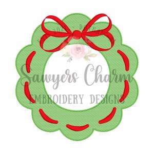 Puede incluir: Corona verde con un lazo rojo y bordes festoneados. La corona tiene un círculo vacío en el centro para personalizar. El texto "Sawyers Charm Embroidery Designs" es visible en el centro de la corona.