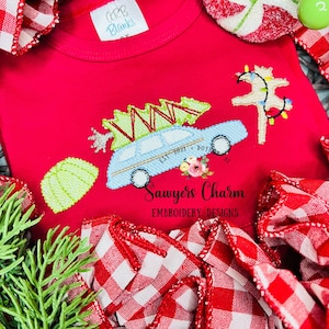 May include: A red t-shirt with an embroidered design of a blue car carrying a Christmas tree, a Christmas tree with lights, and the text "Sawyers Charm Embroidery Designs Est. 2021 DOT AL".