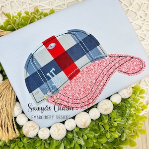 May include: Embroidered design of a red and blue plaid baseball cap with a white initial "J" on the front. The text "Sawyers Charm Embroidery Designs" is below the cap.