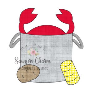 May include: A gray bucket with a red crab on top. The bucket has a white handle and a yellow and white striped object on the side. The bucket also has the text "Sawyers Charm Embroidery Designs" and "Est 2021 Dothan Al" on the side.