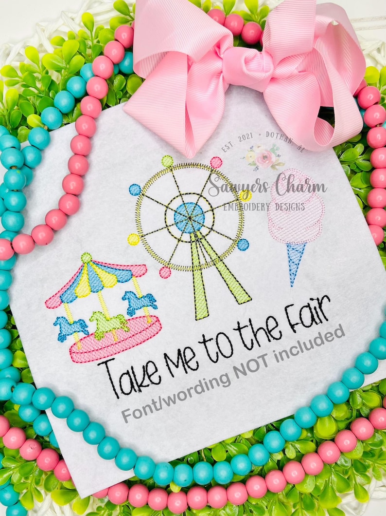 May include: A white square with embroidered fair-themed designs, including a Ferris wheel, carousel, and cotton candy. The text "Take Me to the Fair" is below the designs. A pink bow and beaded garland frame the square.