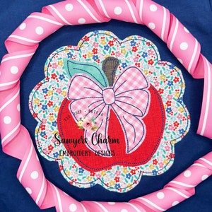 Pode incluir: Uma maçã vermelha com um laço de xadrez rosa e branco e folhas verdes. A maçã é cercada por um desenho floral e o texto "Est. 2021 Dothan, AL Sawyers Charm Embroidery Designs".