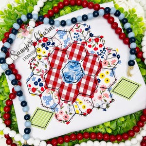 May include: White fabric with a floral and gingham pattern, featuring a central hexagon design. The design is surrounded by red, white, and blue beaded garland and greenery. The text "Sawyers Charm EMBROIDERY" is visible.