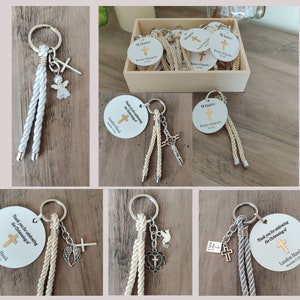 May include: A set of white and beige rope keychains with silver charms, including a cross, angel wings, a dove, and a heart. The keychains are decorated with a round tag that says "Thank you for celebrating the Christening of Landon Hawk".