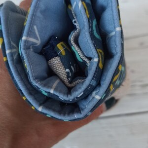 Può includere: Un astuccio per matite in tessuto blu arrotolato con un motivo geometrico bianco e giallo.