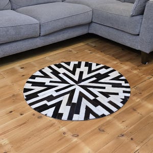 Może przedstawiać: Okrągły dywan z czarno-białej skóry krowiej z geometrycznym wzorem. Dywan wykonany jest z kawałków skóry zszytych ze sobą, tworząc unikalny wzór.