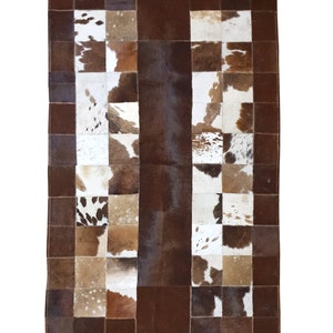 Peut inclure: Un tapis en peau de vache patchwork avec des patchs bruns, blancs et noirs. Le tapis est composé de différentes pièces de peau de vache cousues ensemble pour créer un design unique.