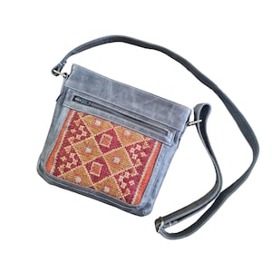 May include: A grey leather crossbody bag with a colourful embroidered patch on the front. The bag has a zip closure and a long adjustable strap.