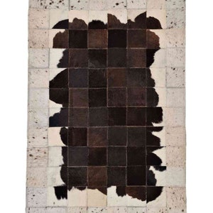 Peut inclure: Un tapis en peau de vache patchwork avec un motif noir et blanc. Le tapis est composé de carrés de différentes tailles et couleurs, et les bords sont cousus ensemble.