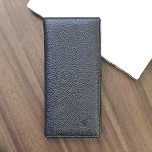 Op de afbeelding: Een donkergrijze leren portemonnee met een getextureerd oppervlak. De rechthoekige portemonnee lijkt gesloten. Hij ligt op een houten oppervlak. Een witte laptop is op de achtergrond te zien.