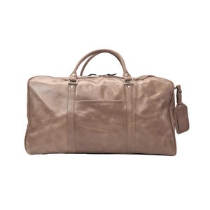 May include: A large, taupe leather duffel bag with two top handles and a front pocket. The bag features a luggage tag and metal hardware. This travel bag has a classic design and is made from a soft, supple leather. The bag measures approximately 60cm in length.