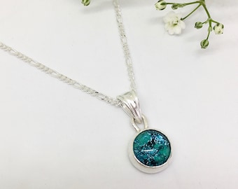 May include: A silver chain necklace with a small round pendant featuring a teal blue dichroic glass inlay.