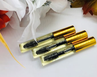 May include: Three gold-colored tubes of clear lash growth serum with black applicator brushes. The tubes are stacked on top of each other.