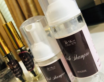 May include: Two clear plastic bottles with white pumps and black labels. The labels read "The NK Collection" and "Lash Shampoo - Hypoallergenic".