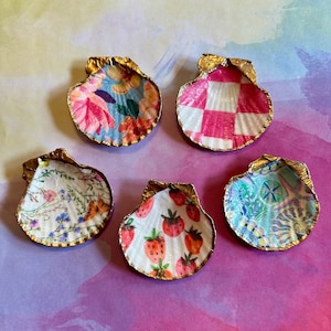 May include: Five decorative seashells with gold trim and various patterned designs. The shells are decorated with floral, chequered, strawberry, and abstract patterns.