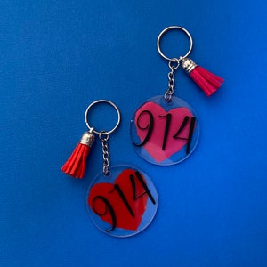 May include: Two keychains with red heart-shaped charms and black numbers "914" printed on them. The keychains have silver key rings and red tassels.