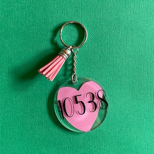 May include: Pink heart-shaped keychain with a silver chain and tassel. The heart has the number 10538 printed on it.