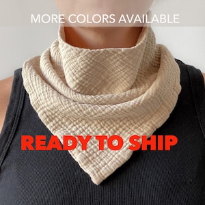 May include: A beige cotton neck scarf with a diamond pattern. The scarf is folded and worn around the neck. The text "READY TO SHIP" is printed in red on the scarf.